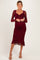woman wearing a burgundy maternity dress with long sheer sleeves and a ruffled hem, showcasing her baby bump
