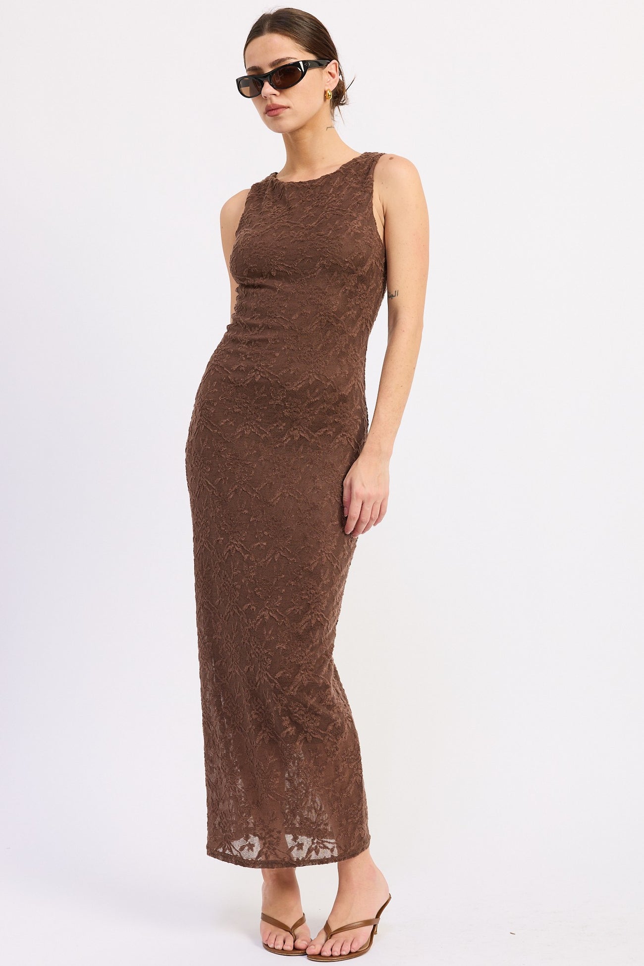 woman wearing a brown lace maxi dress with a fitted silhouette and sunglasses, posing sideways