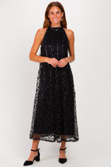 woman wearing a black halter neck midi dress with sequin details and a sheer overlay, styled with black heels