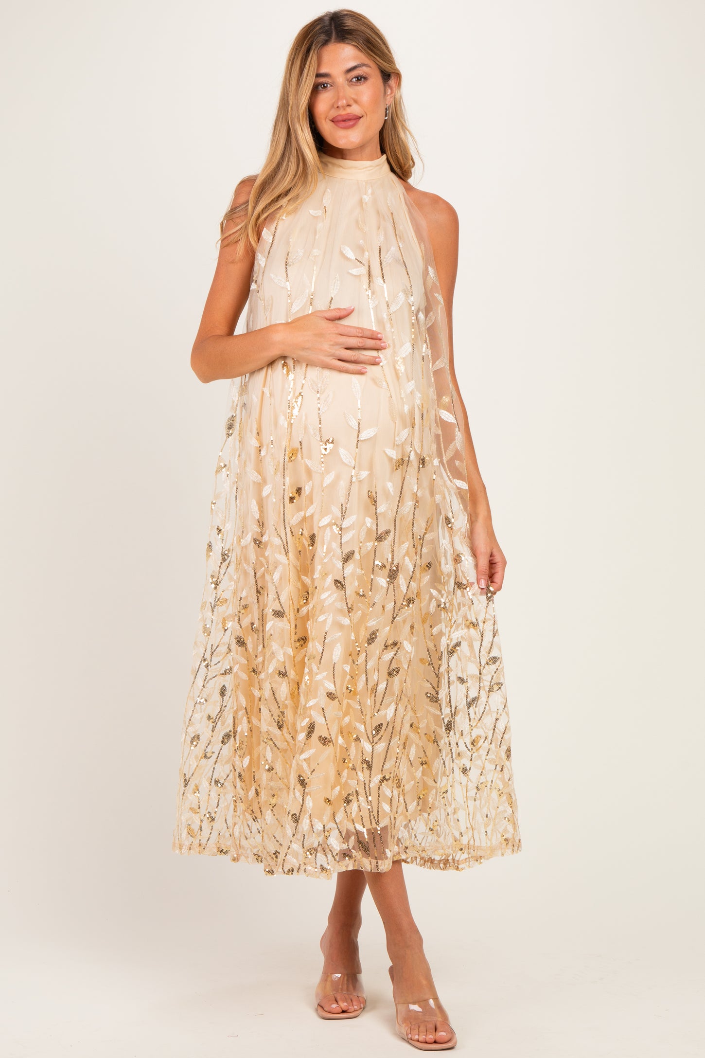 woman wearing a flowy beige maternity dress with floral embroidery, gently cradling her baby bump