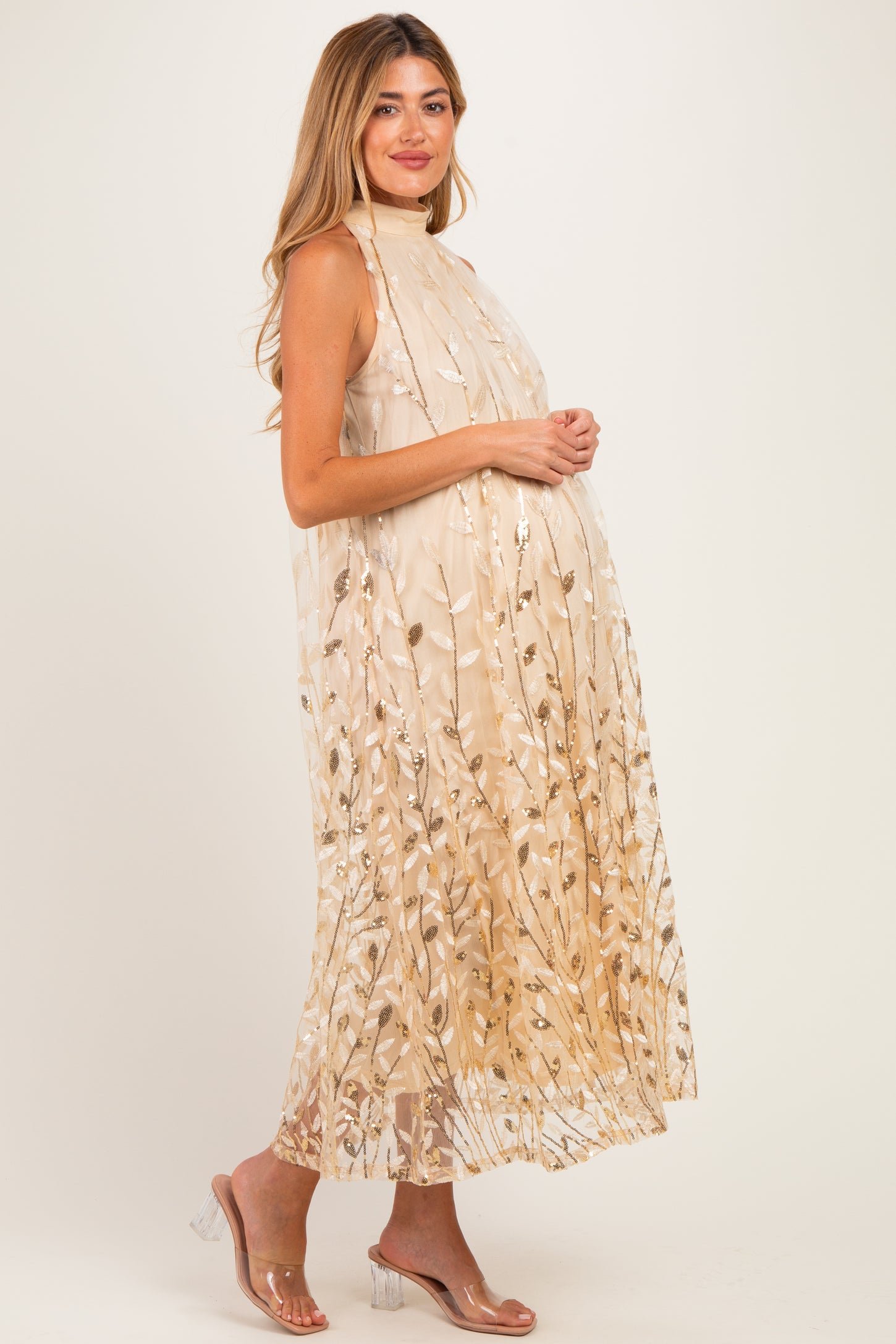woman wearing a cream maternity dress with gold floral details and a flowing silhouette, showcasing her baby bump