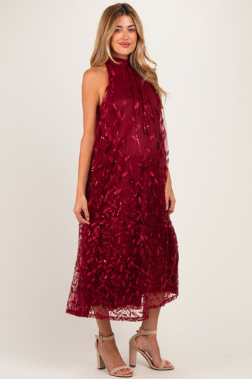 woman wearing a burgundy sleeveless maternity dress with floral embroidery and a flowing silhouette, showcasing her baby bump
