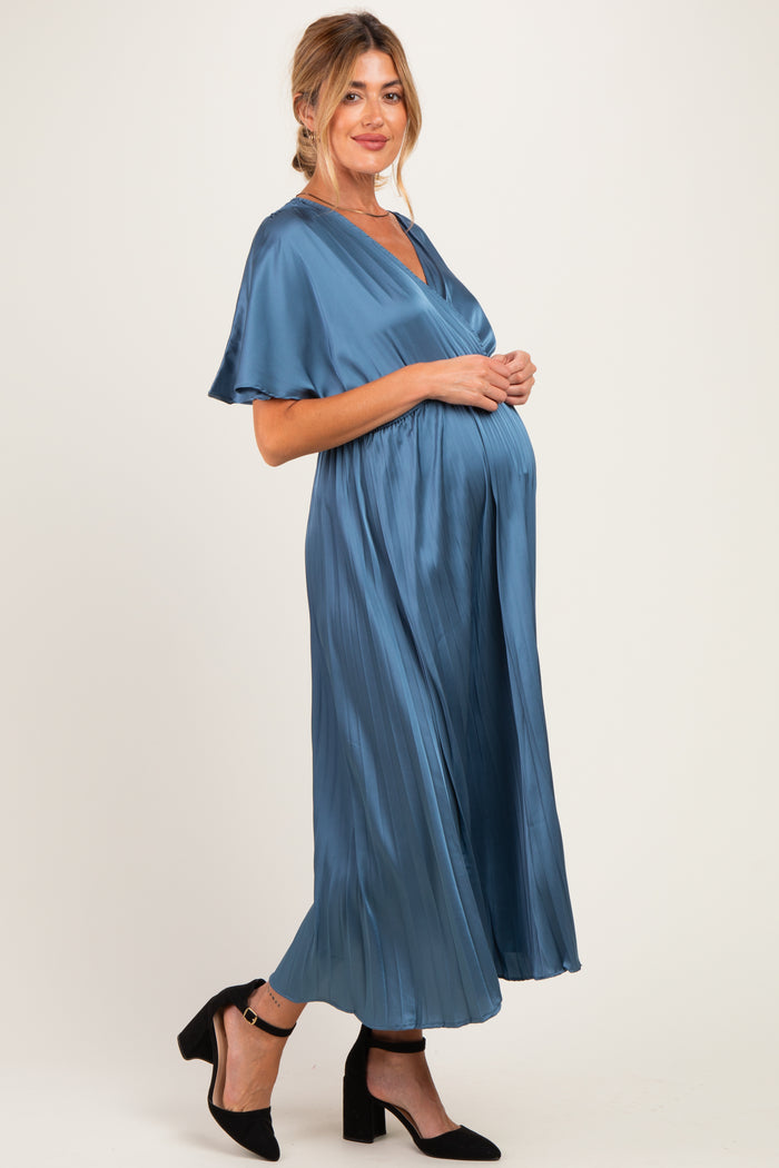 woman wearing a blue satin maternity dress with flutter sleeves and a flowing skirt, highlighting her baby bump