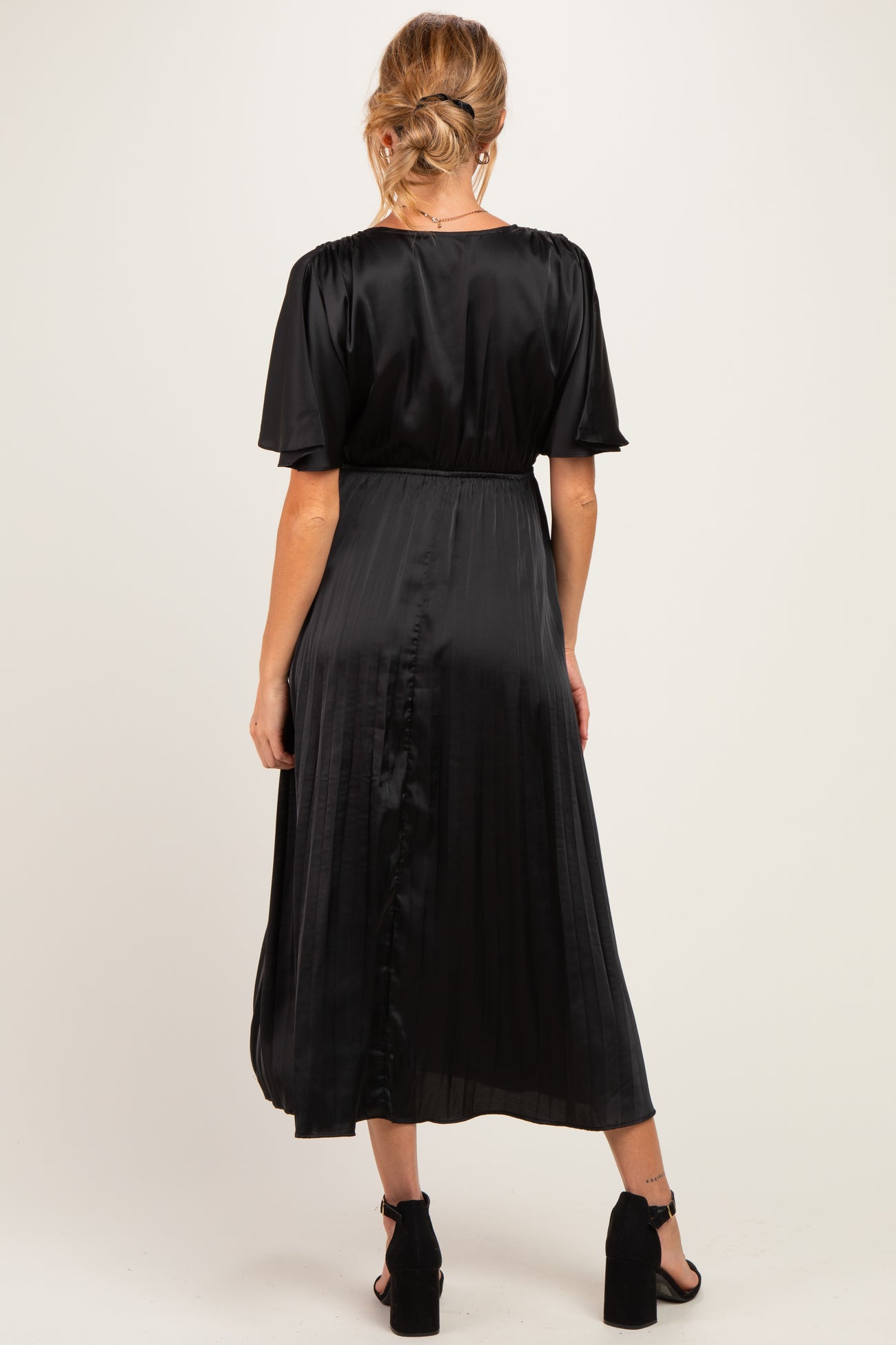 woman wearing a black satin maternity dress with short sleeves and a pleated skirt, showing a baby bump from the back