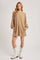 woman wearing a tan long sleeve oversized dress with pockets and white cowboy boots