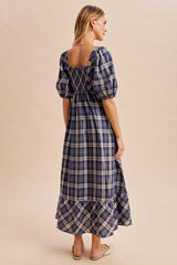 woman wearing a navy blue and white plaid maxi dress with puff sleeves and a smocked back detail