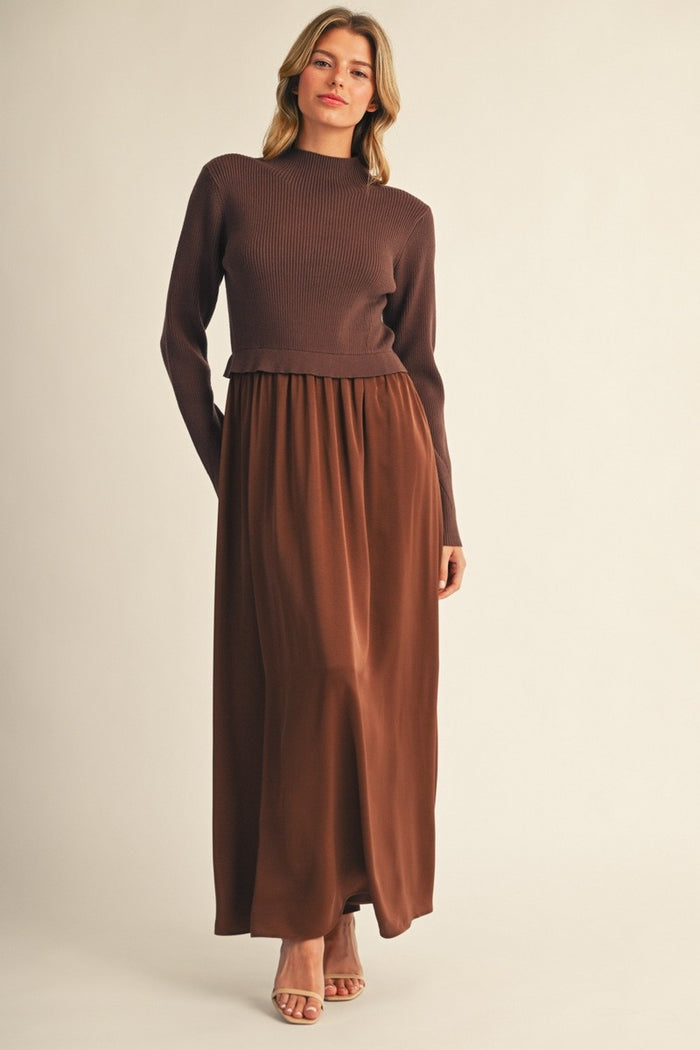 woman wearing a brown ribbed long sleeve top and a brown maxi skirt, standing against a plain background