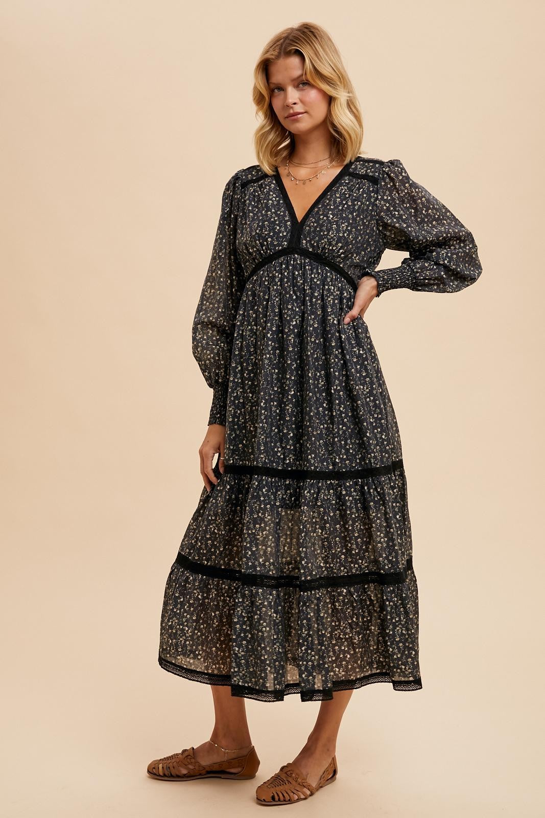 woman wearing a black floral midi dress with tiered layers and puff sleeves, styled with flat sandals