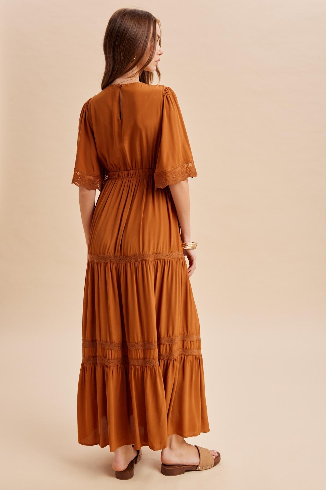 woman wearing a rust-colored maxi dress with lace details and a tiered hem, viewed from the back