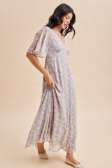 woman wearing a lilac floral maxi dress with flutter sleeves and a v-neckline, standing on a light background