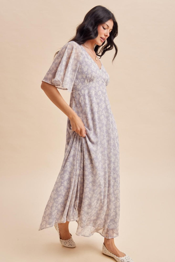 woman wearing a lilac floral maxi dress with flutter sleeves and a v-neckline, standing on a light background