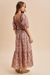 woman wearing a pink floral maxi dress with puff sleeves and a tiered skirt, standing with her back to the camera