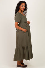 woman wearing a green striped maternity maxi dress with short sleeves and pockets, showing her baby bump