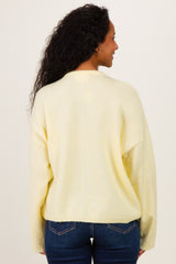 woman wearing a pale yellow oversized maternity sweater with long sleeves and back view, styled with blue jeans
