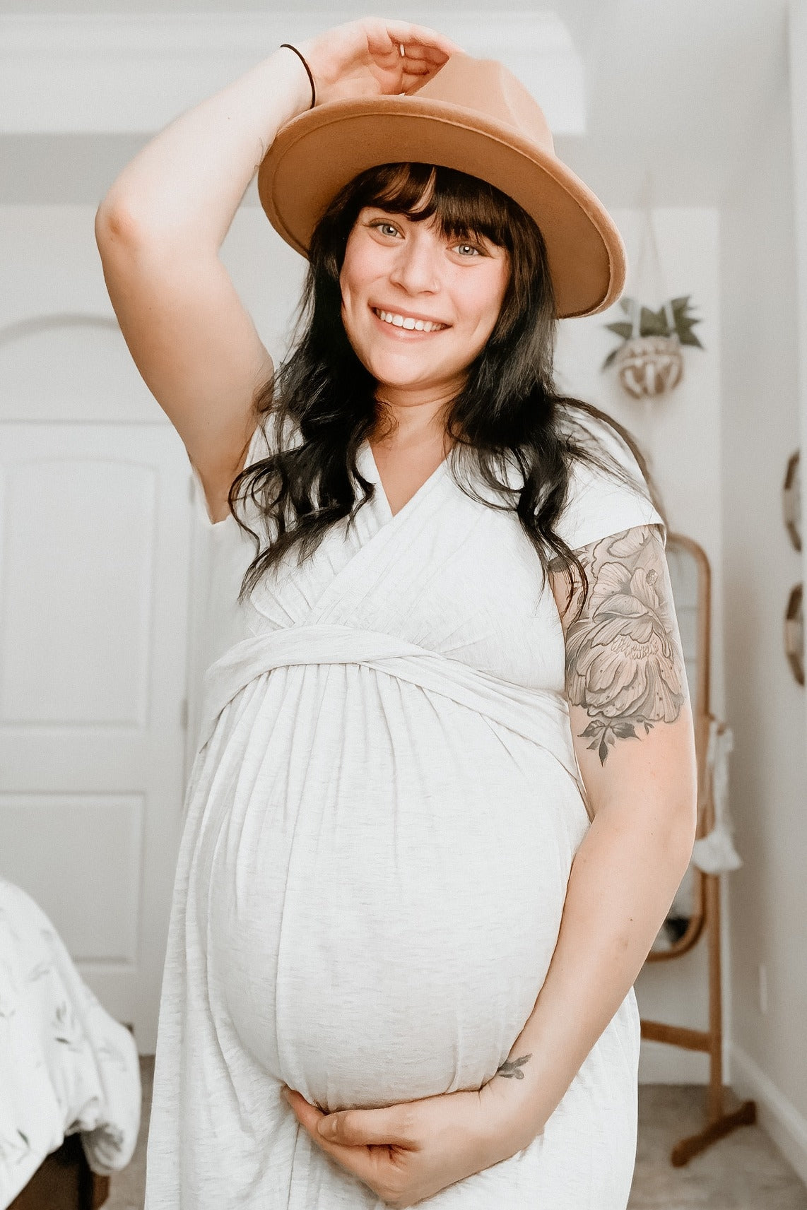woman wearing a light gray maternity wrap dress and holding her baby bump while smiling
