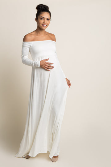 woman wearing a white long sleeve maternity dress, holding her baby bump in an outdoor setting with tall grass