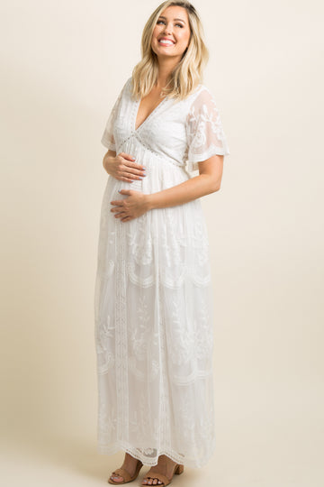 woman wearing a white maternity dress with embroidered details and a flowy silhouette, showing her baby bump