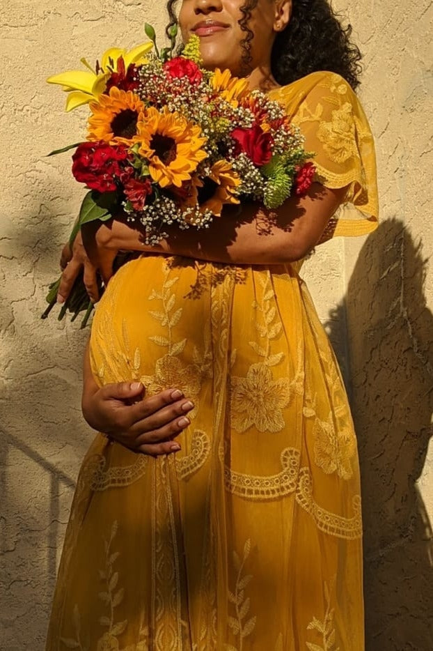 woman wearing a yellow floral maternity dress, holding a bouquet of flowers and cradling her baby bump