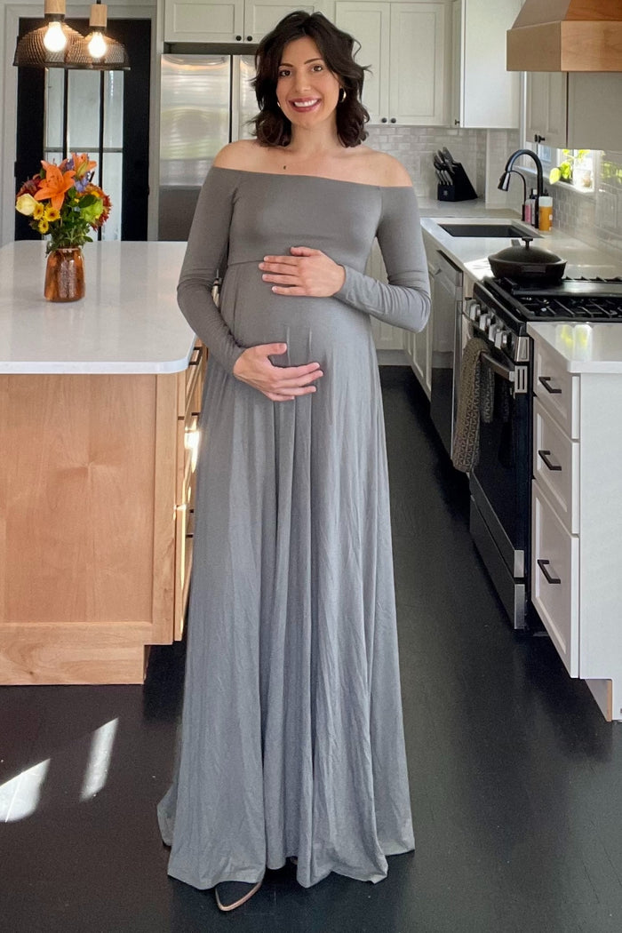 woman wearing a long sleeve gray maternity dress and holding her baby bump in a kitchen setting
