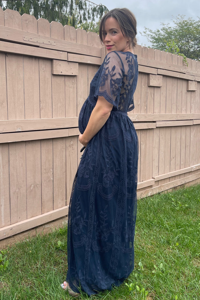 woman wearing a navy blue maternity gown with lace detailing and a visible baby bump