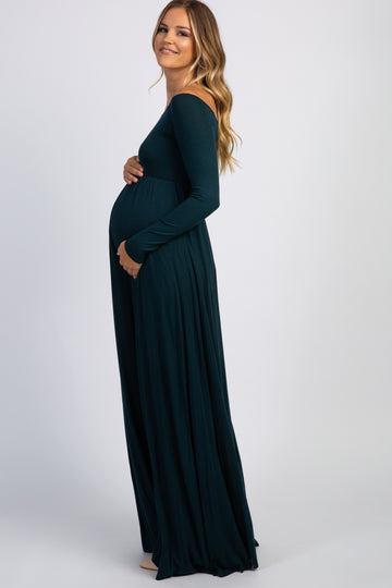 woman wearing a dark green off-shoulder maternity gown and holding her baby bump