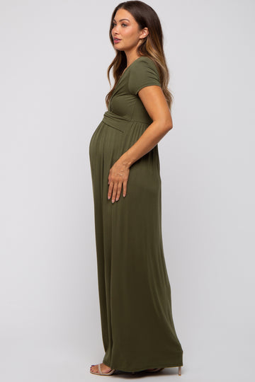 woman wearing a dark green maternity maxi dress with a fitted bodice and flowy skirt, highlighting her baby bump
