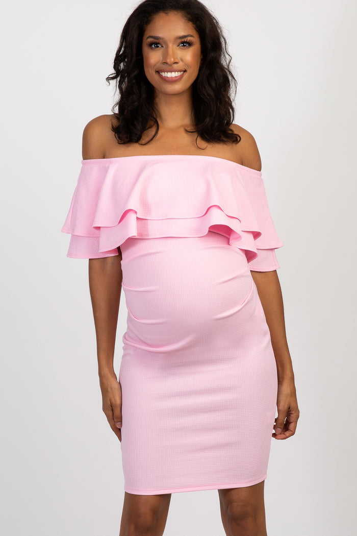 woman wearing a light pink off-shoulder maternity dress, cradling her baby bump at a celebration event