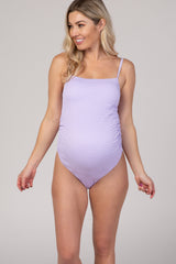 woman wearing a lavender maternity one-piece swimsuit with ruching and adjustable straps, showing her baby bump