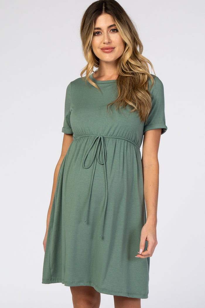 woman wearing a sage green short sleeve maternity dress with a drawstring waist and flowing skirt