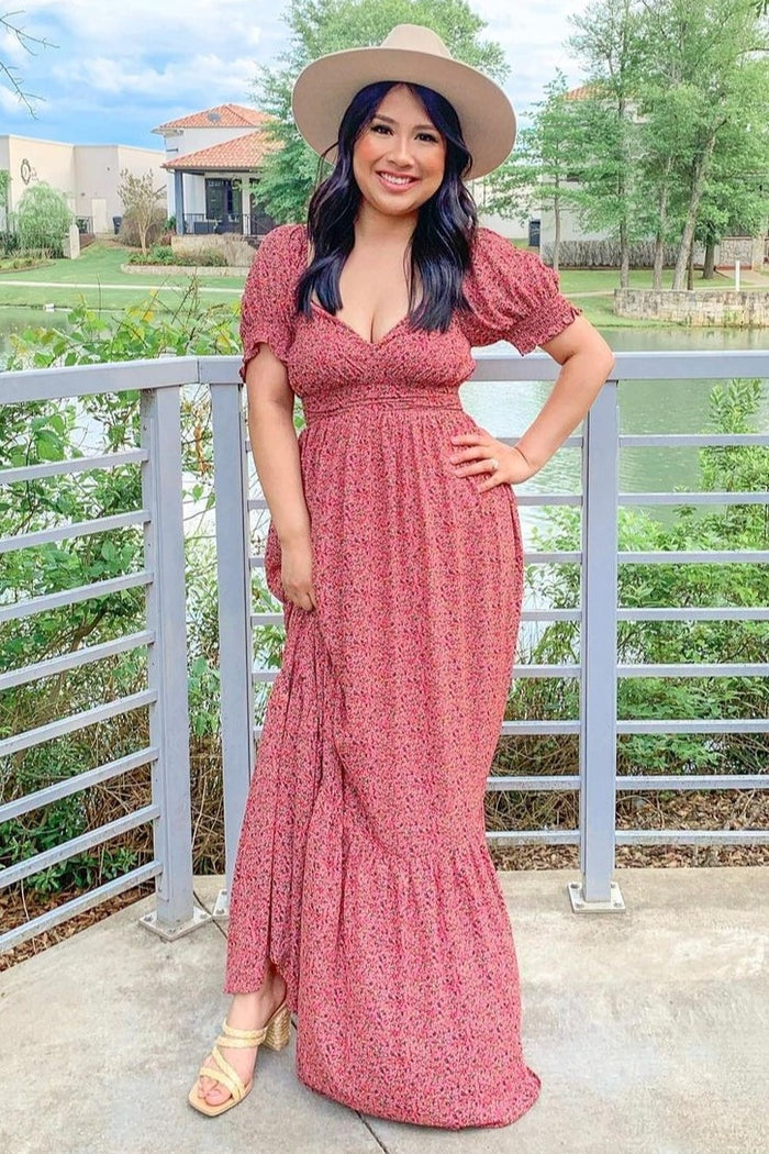 woman wearing a pink floral maxi dress with puff sleeves and a fitted waist, styled with a wide-brimmed hat