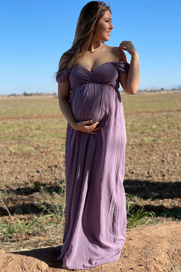 woman wearing a lavender off-the-shoulder maternity gown and holding her baby bump in a scenic outdoor setting