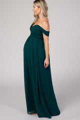 woman wearing a dark green off-the-shoulder maternity gown with a flowing skirt and visible baby bump