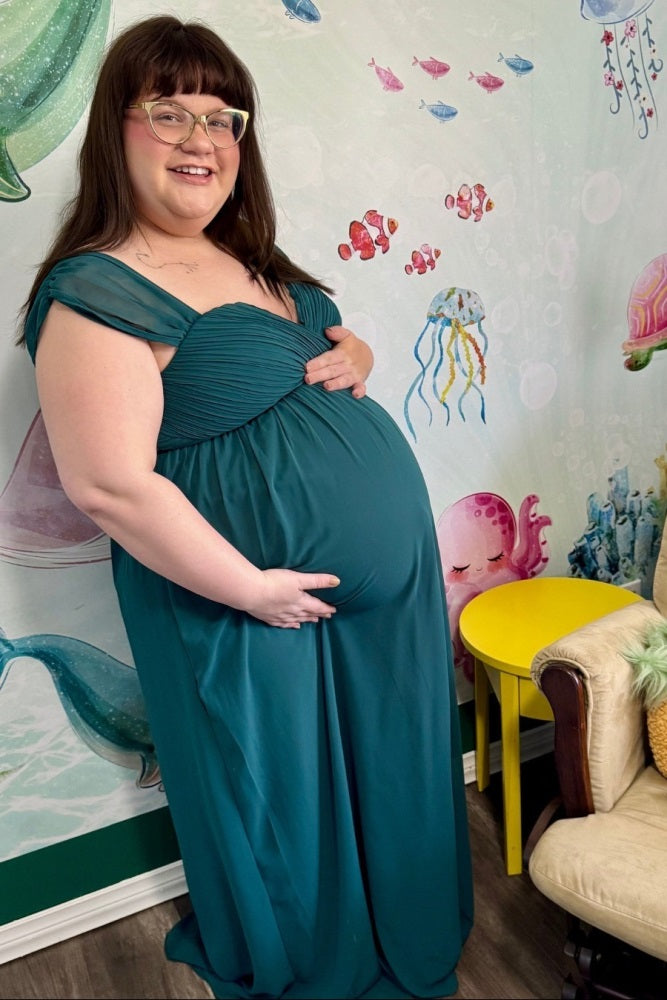 woman wearing a teal maternity gown with gathered bodice, holding her baby bump