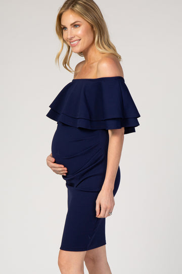 woman wearing a navy off-the-shoulder maternity dress with layered ruffles and a visible baby bump