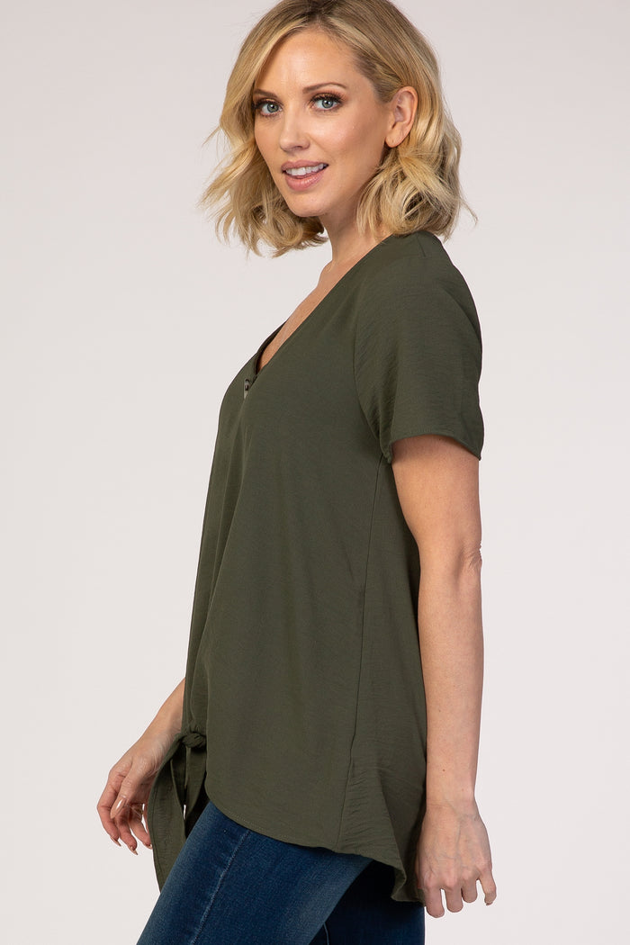 woman wearing an olive green short sleeve top with a v-neck and side tie detail, paired with blue jeans