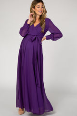 woman wearing a purple long sleeve maternity dress with a tie waist and flowing skirt, featuring a visible baby bump