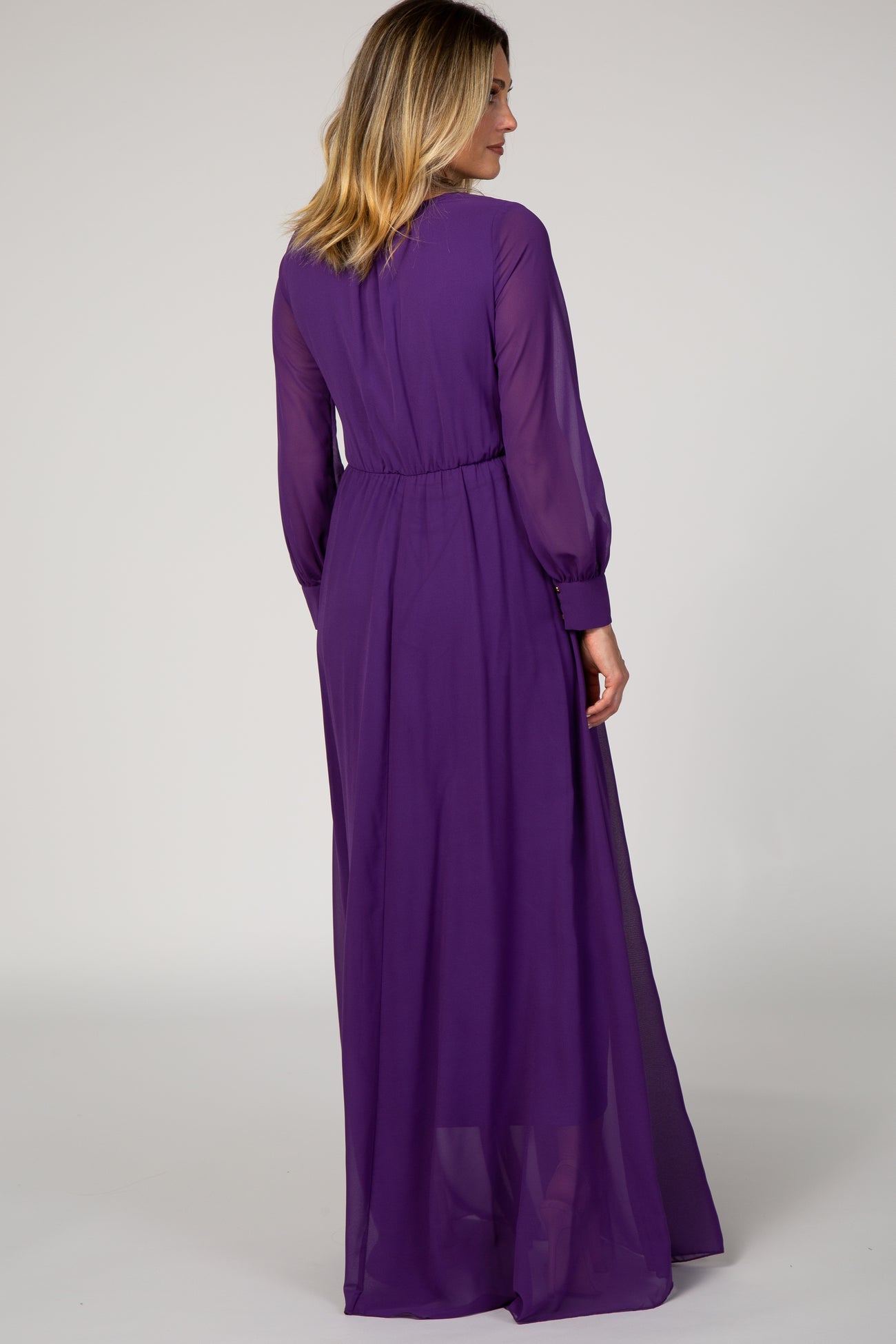 woman wearing a long sheer purple maxi dress with long sleeves and cinched waist, shown from the back