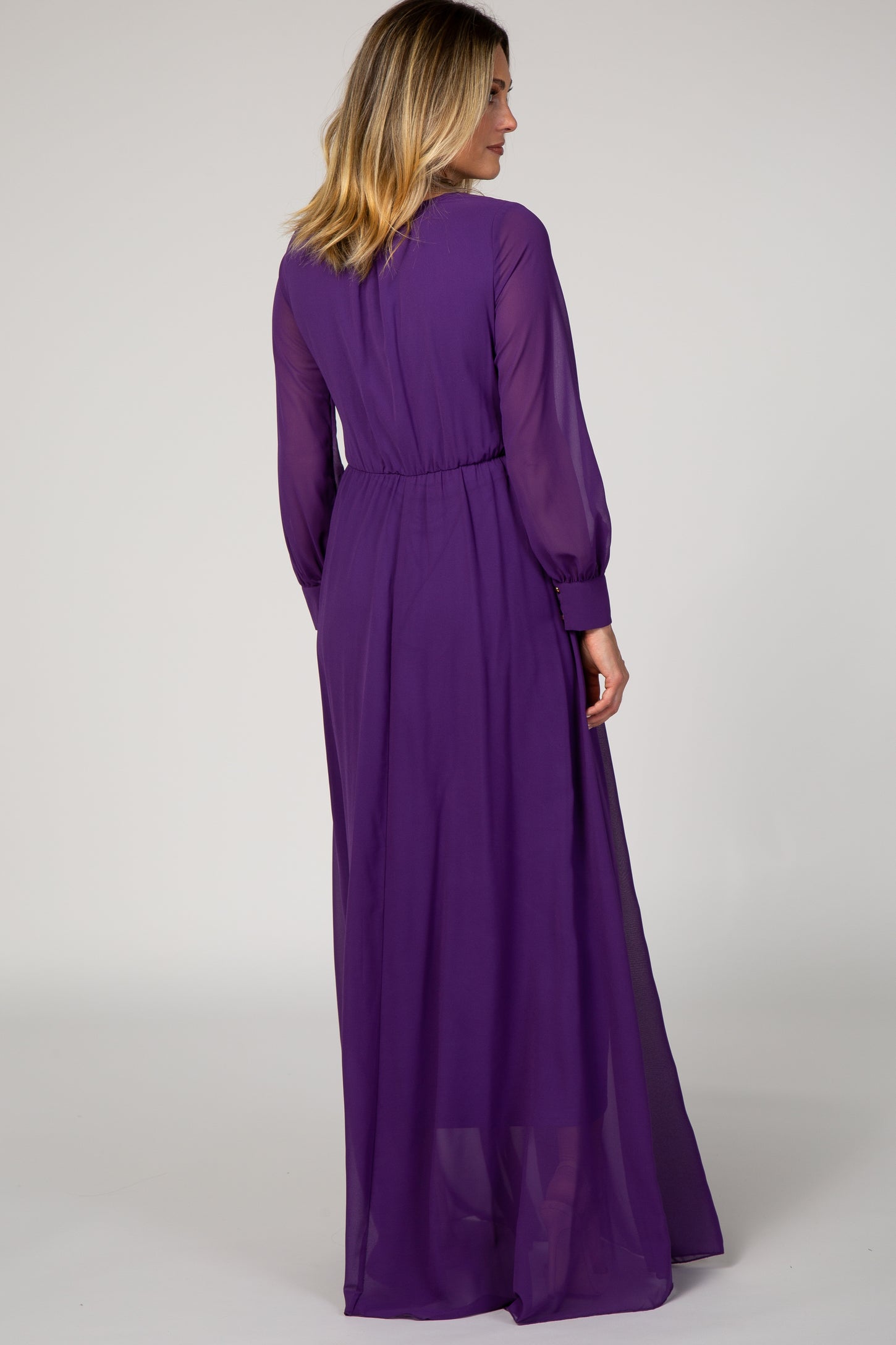 woman wearing a long sheer purple maxi dress with long sleeves and cinched waist, shown from the back
