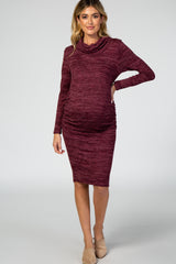 woman wearing a burgundy long sleeve maternity dress with a cowl neck and side ruching, showcasing her baby bump