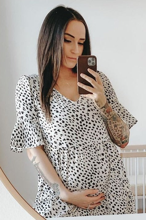 woman wearing a black and white spotted maternity dress and holding her baby bump in front of a mirror