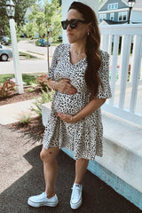 pregnant woman in black and white spotted maternity dress and white sneakers standing on a porch