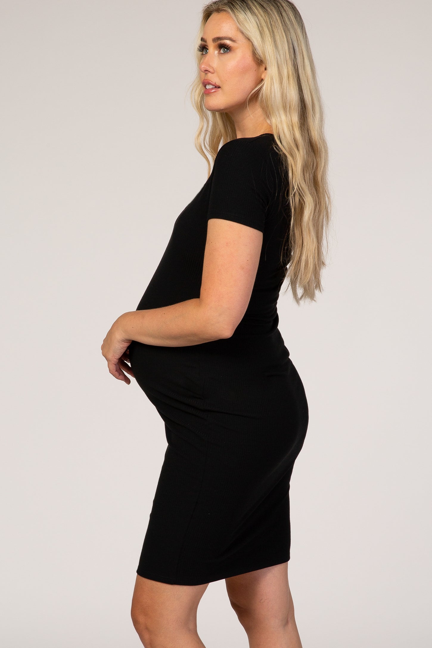 pregnant woman with blonde hair wearing a black short sleeve maternity dress against a white background