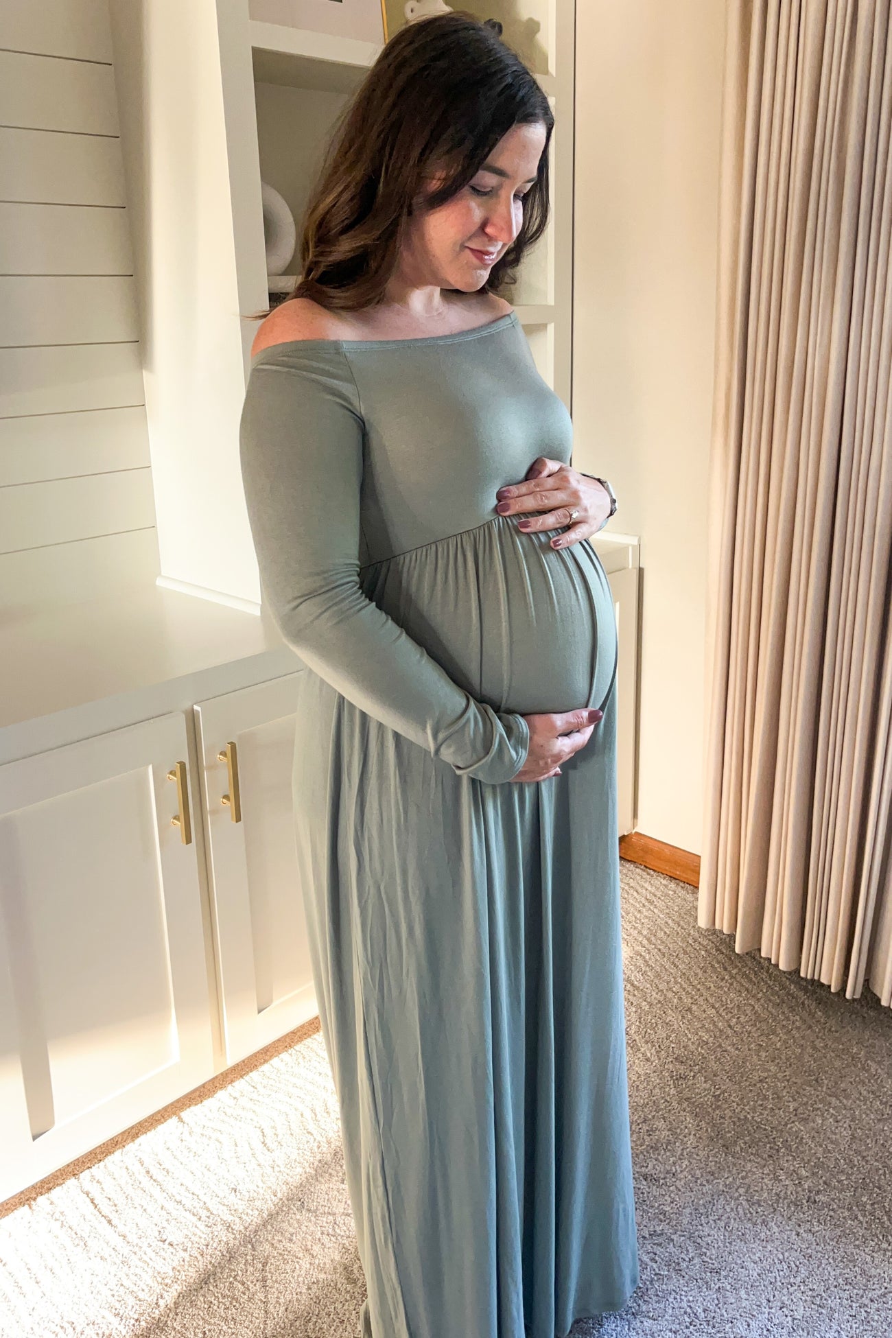 woman wearing a soft green off-the-shoulder maternity dress and cradling her baby bump