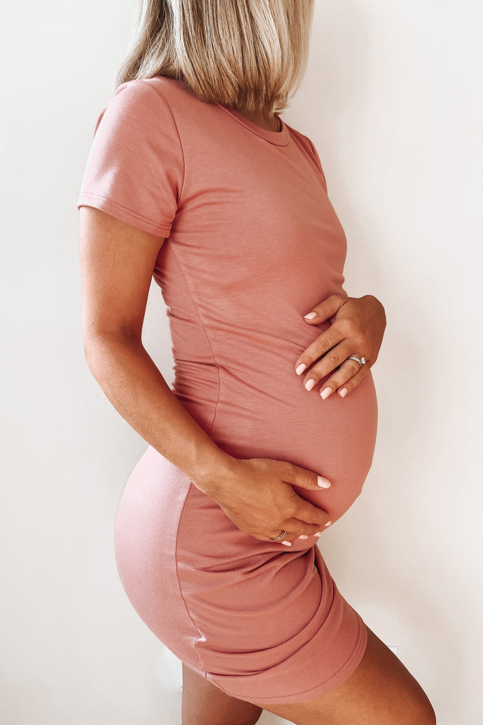 woman wearing a dusty rose short sleeve maternity dress and holding her baby bump