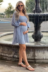woman wearing a light blue maternity dress with puff sleeves and holding her baby bump by a fountain