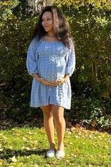 woman wearing a light blue maternity dress with puff sleeves and holding her baby bump in a garden setting