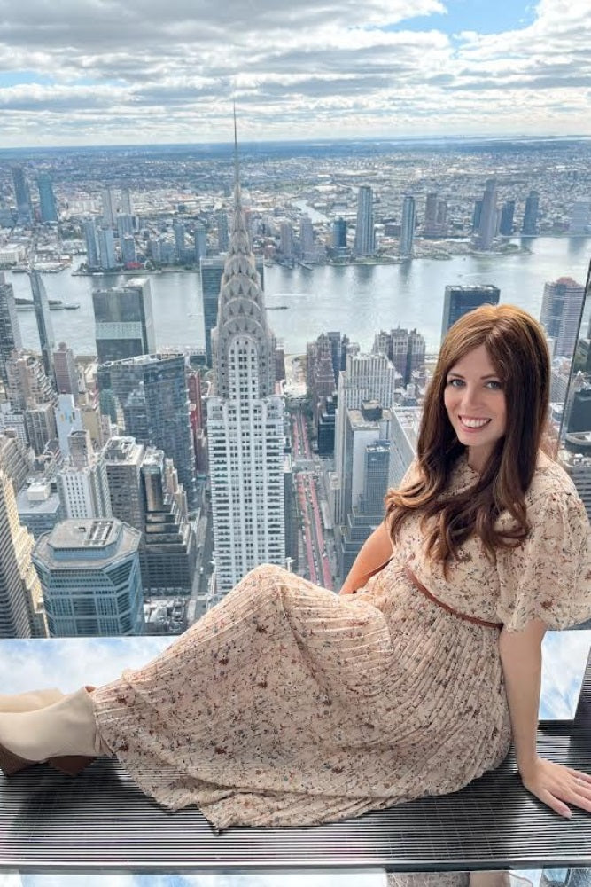 woman sitting on an observation deck wearing a light beige floral maxi dress with short sleeves and a pleated skirt