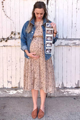woman wearing a floral maternity dress with a denim jacket, holding ultrasound photos and showing her baby bump