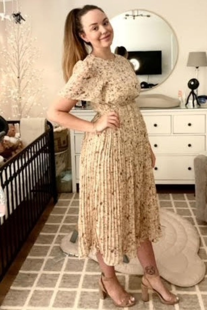 woman wearing a floral midi dress with puff sleeves and a pleated skirt, standing beside a crib in a nursery