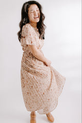 woman wearing a floral midi dress with short sleeves and a cinched waist, smiling and twirling in the dress